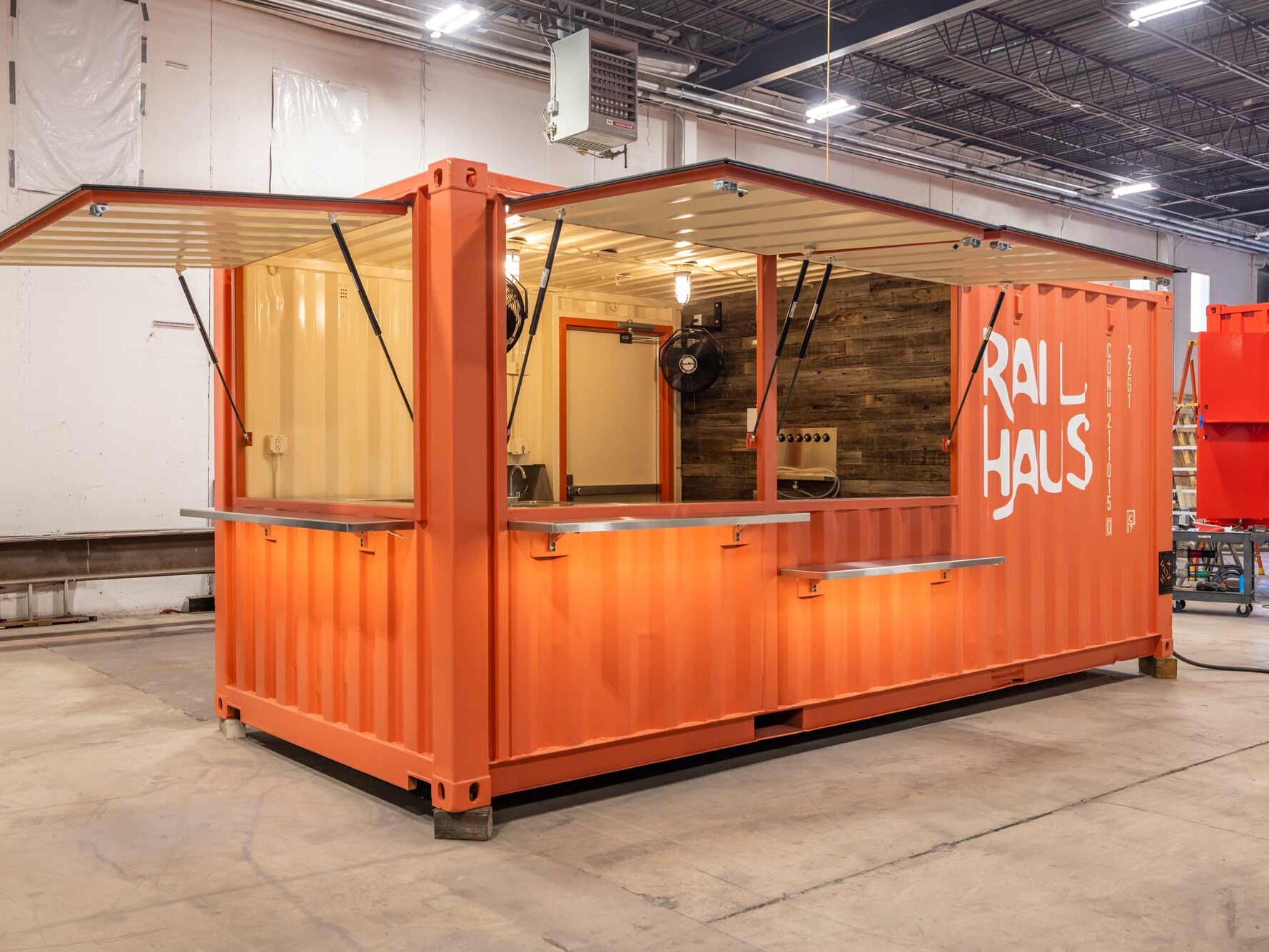 coral shipping container bar with three awnings and eight taps reclaimed wood wall with cage lights and walk in cooler for client named Rail Haus
