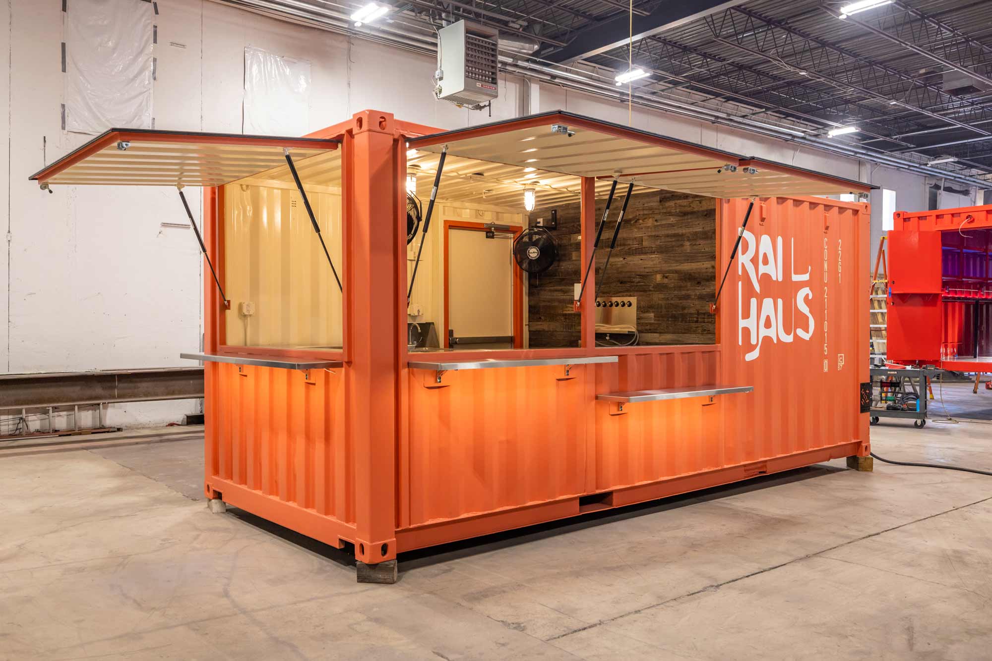 coral shipping container bar with three awnings and eight taps reclaimed wood wall with cage lights and walk in cooler for client named Rail Haus